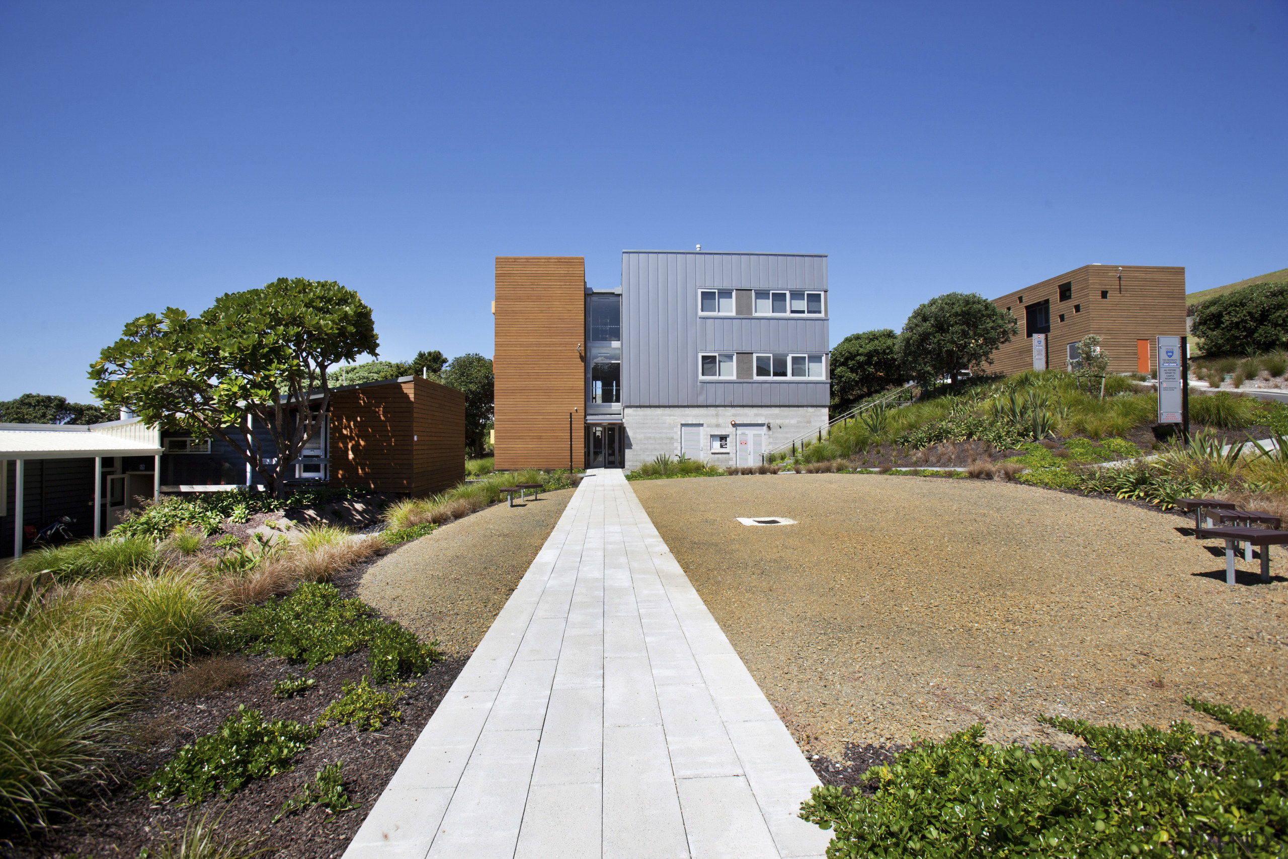 View of path to building with landscaping. - apartment, architecture, building, campus, cottage, estate, facade, grass, home, house, neighbourhood, property, real estate, residential area, sky, suburb, blue