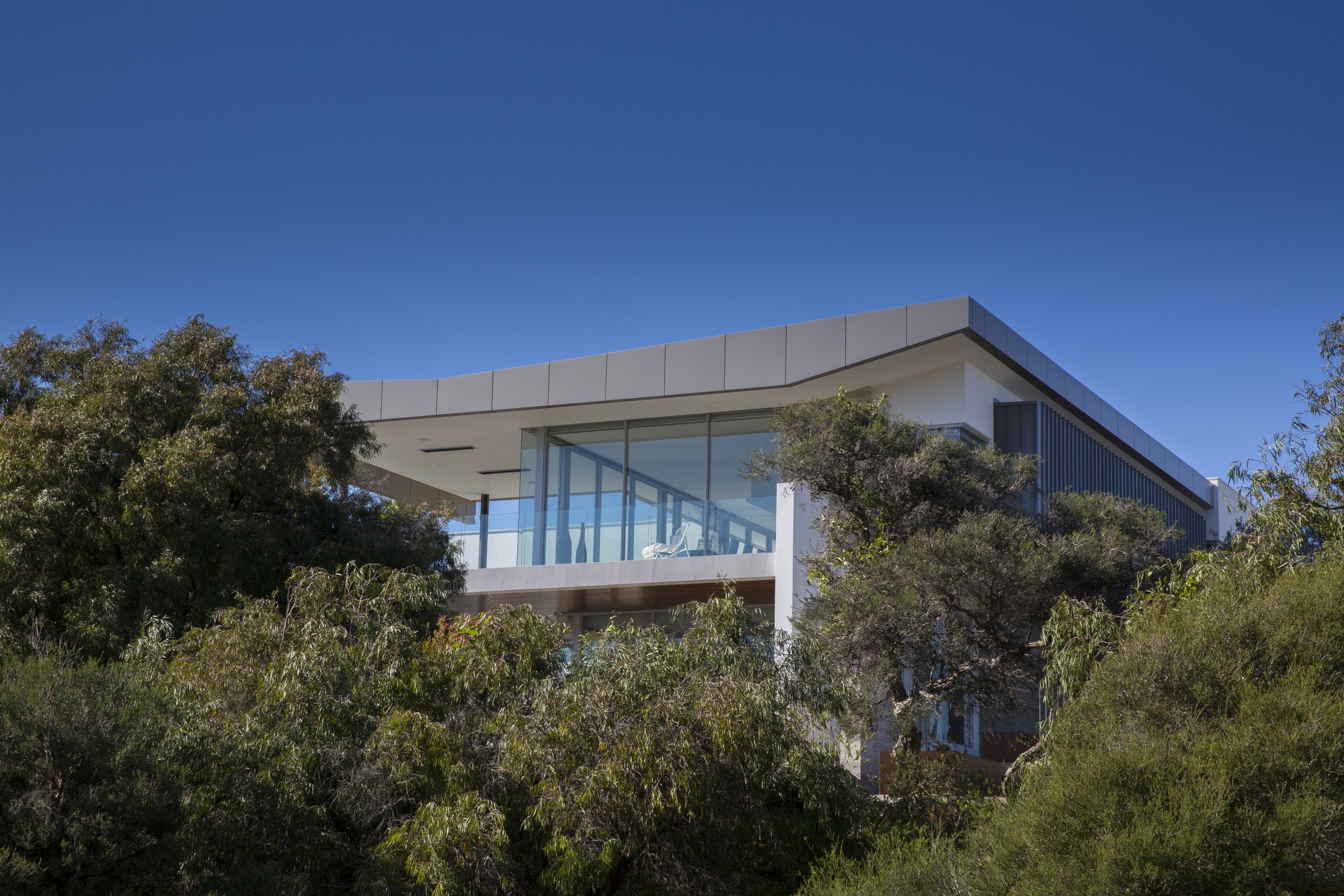 Seen rising above the treeline, this coastal home architecture, building, corporate headquarters, cottage, daytime, estate, facade, home, house, property, real estate, residential area, roof, sky, tree, villa, blue, brown