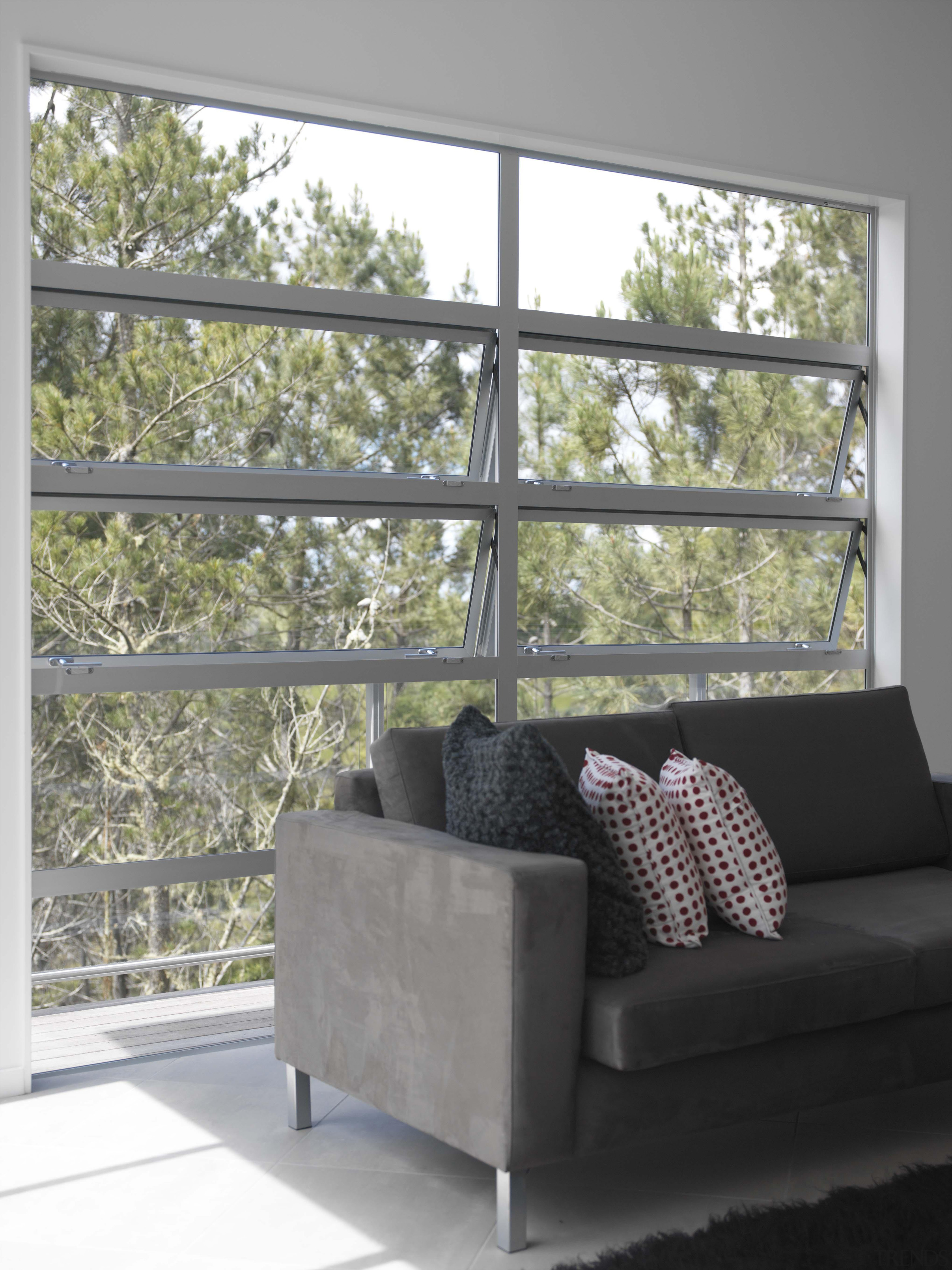 Awning windows symmetrically frame the outdoor treescape. chair, couch, daylighting, furniture, home, house, interior design, living room, loveseat, sofa bed, wall, window, window covering, window treatment, gray