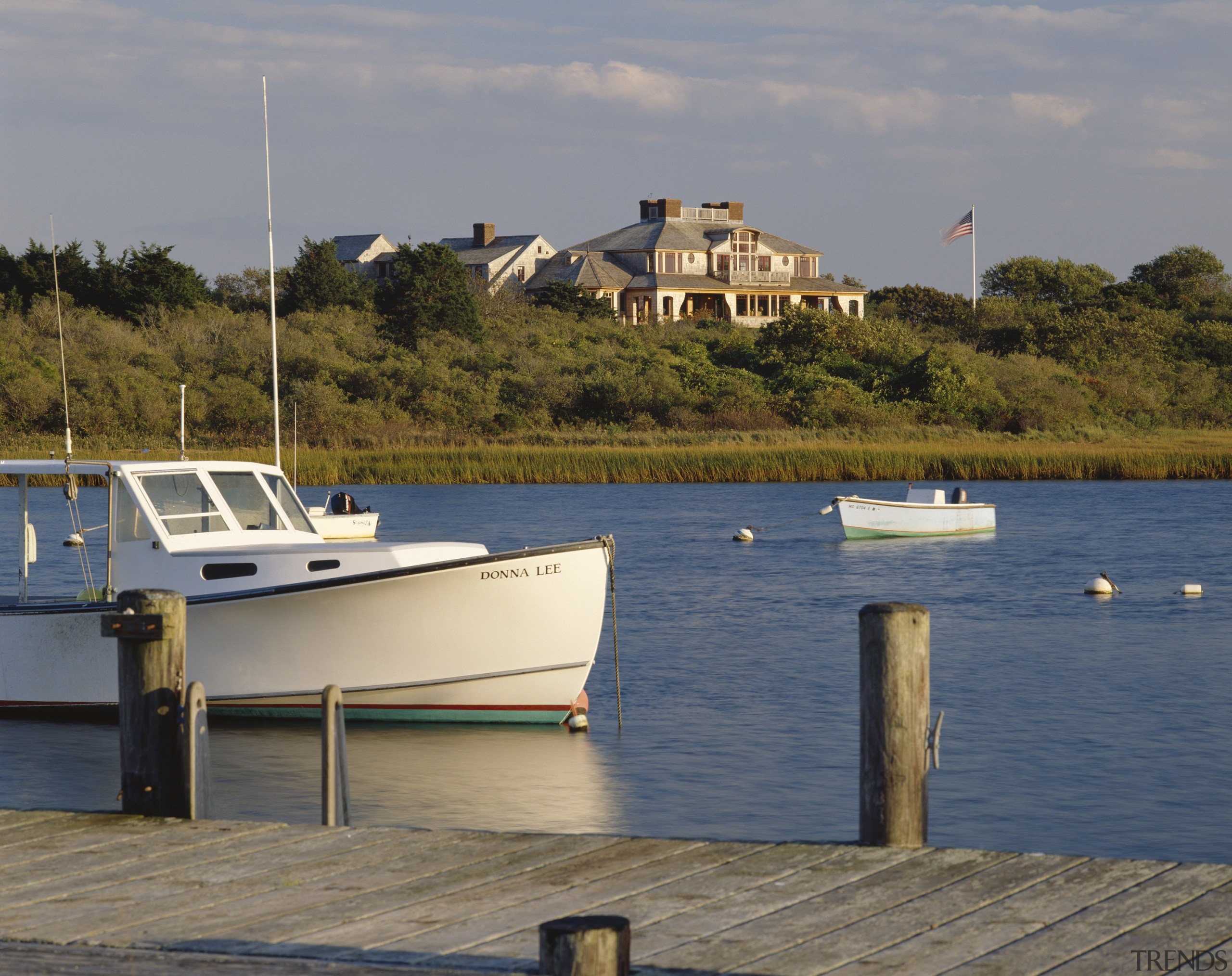 Exterior view of cottage beyond the water way. boat, boating, body of water, coast, coastal and oceanic landforms, dock, harbor, marina, ocean, recreation, sea, shore, sky, tree, vehicle, water, watercraft, waterway, gray