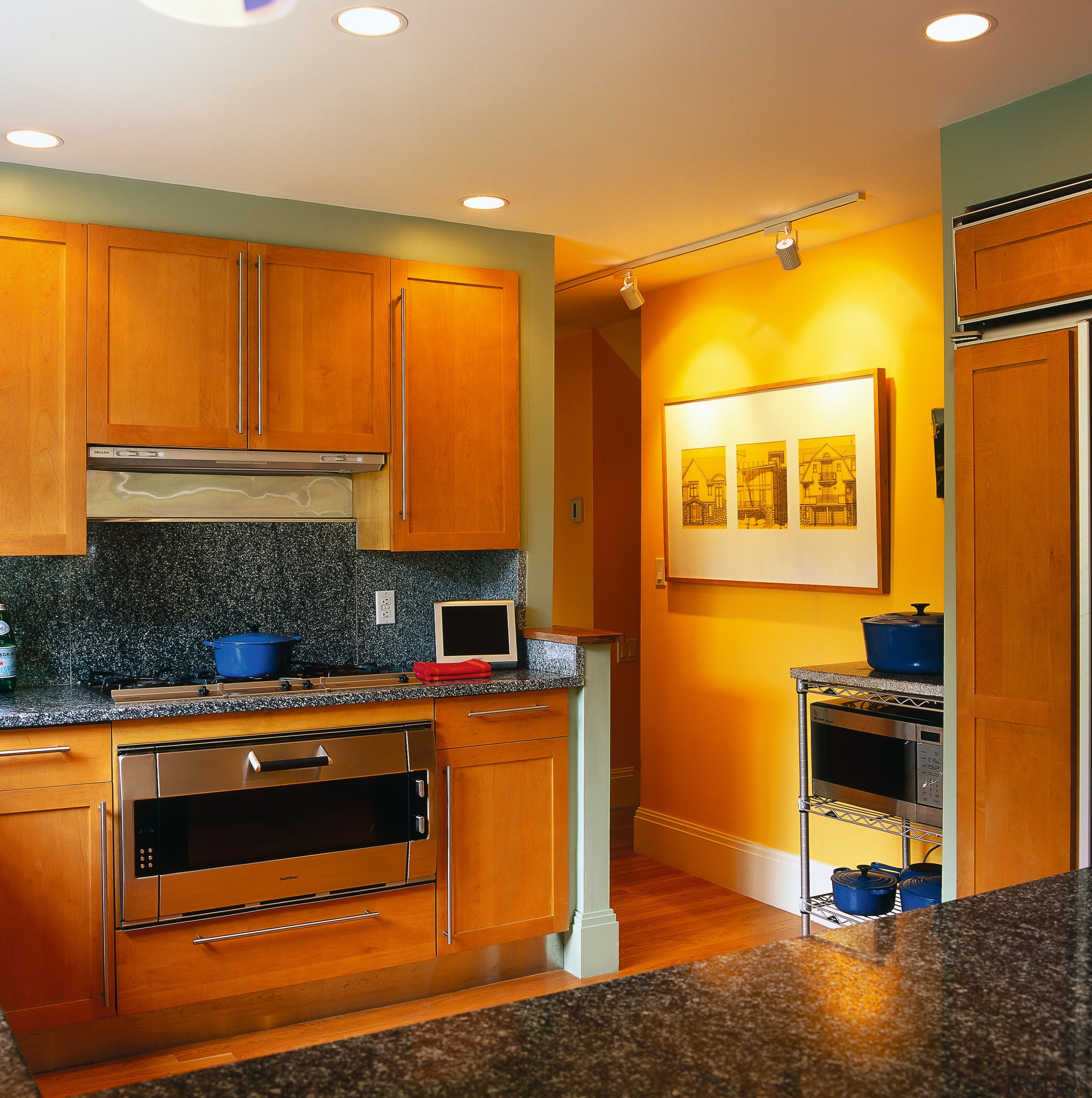 View of the kitchen area with wood cabinetry, cabinetry, ceiling, countertop, floor, flooring, hardwood, home, interior design, kitchen, living room, real estate, room, under cabinet lighting, wall, wood flooring, brown, orange