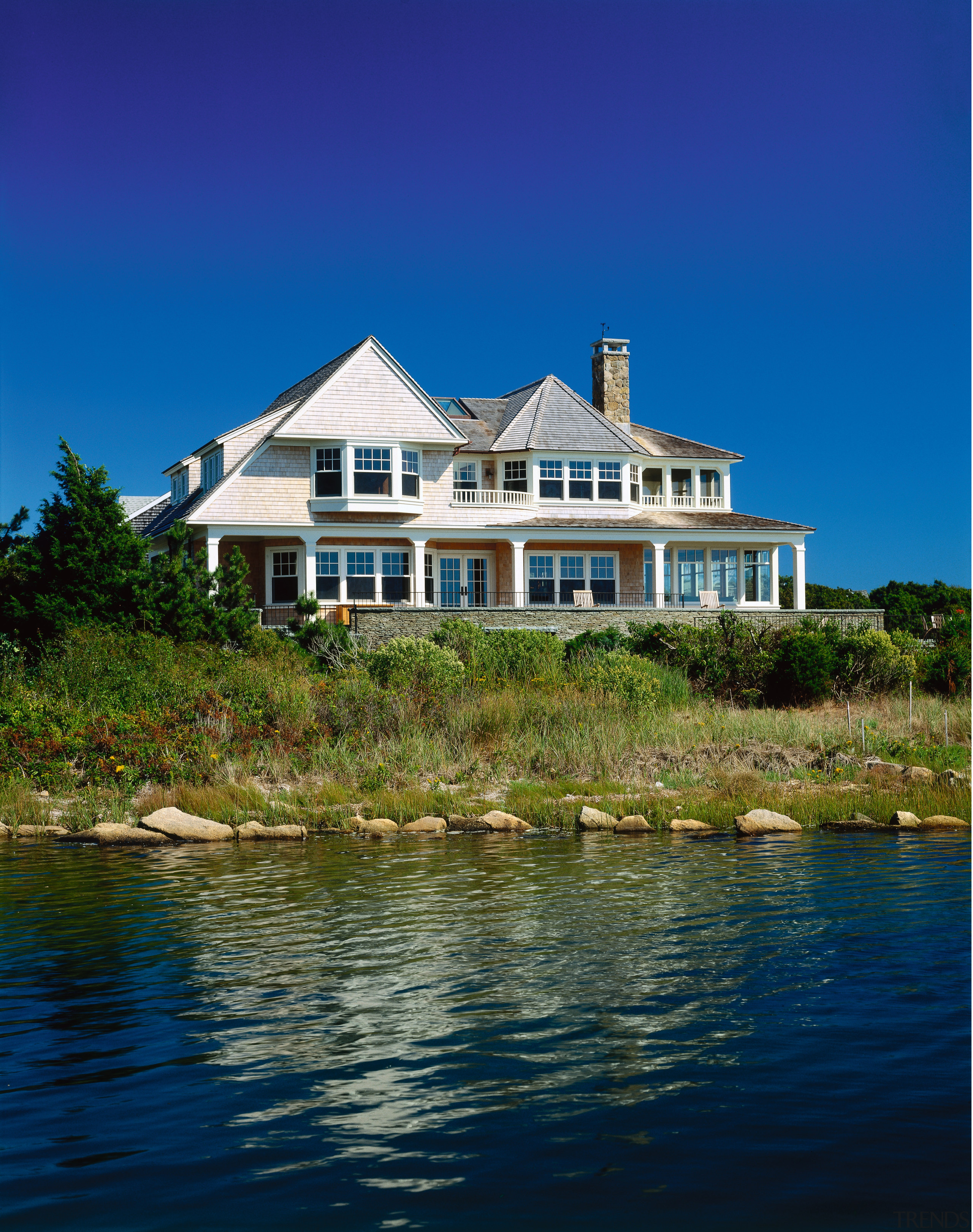 view of this cape cod home situated on building, cottage, estate, facade, home, house, lake, mansion, property, real estate, reflection, sea, sky, tree, water, waterway, blue