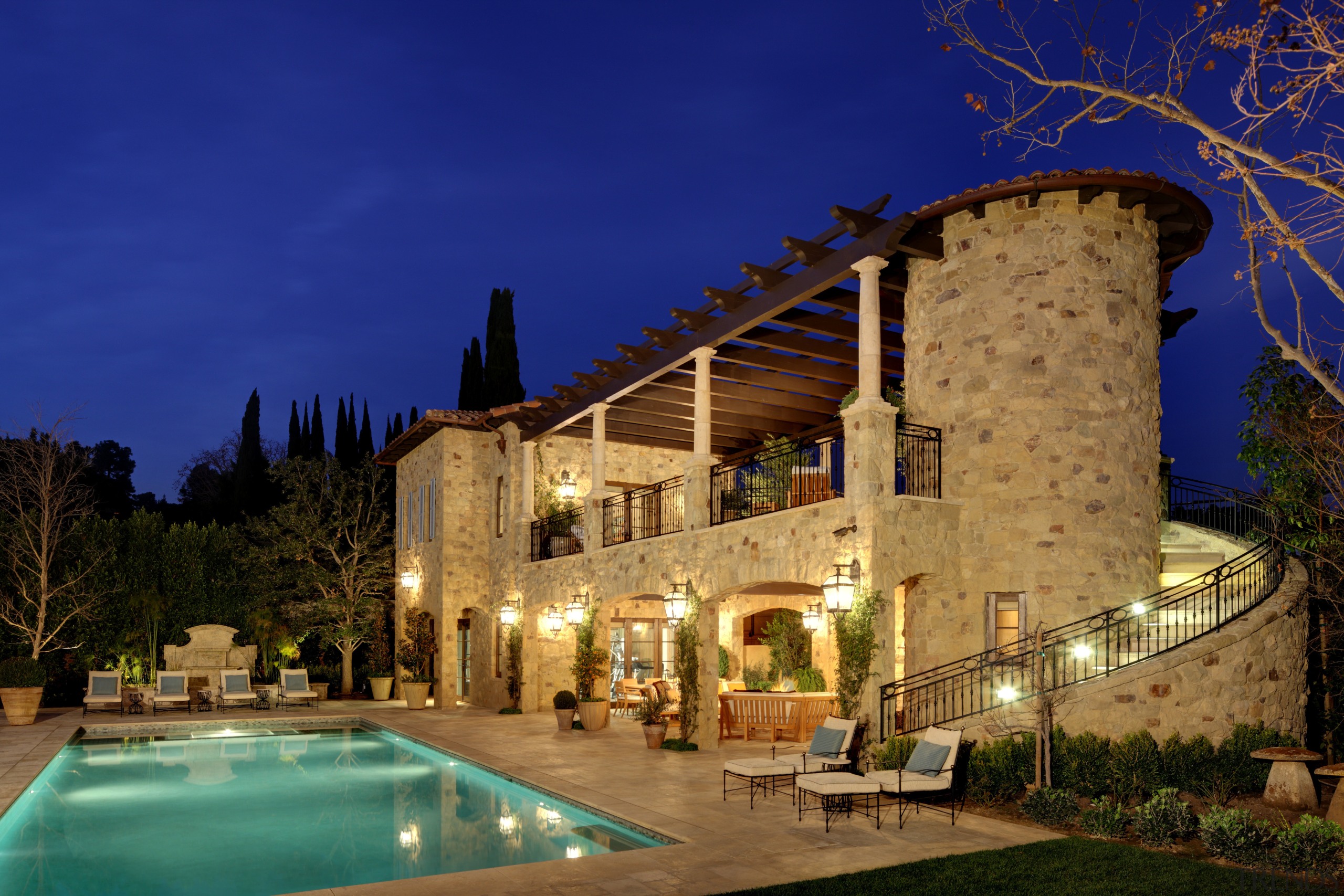 The rustic guest house includes a balcony, covered architecture, building, estate, evening, hacienda, home, hotel, house, landscape lighting, lighting, mansion, night, property, real estate, reflection, sky, villa, blue, brown