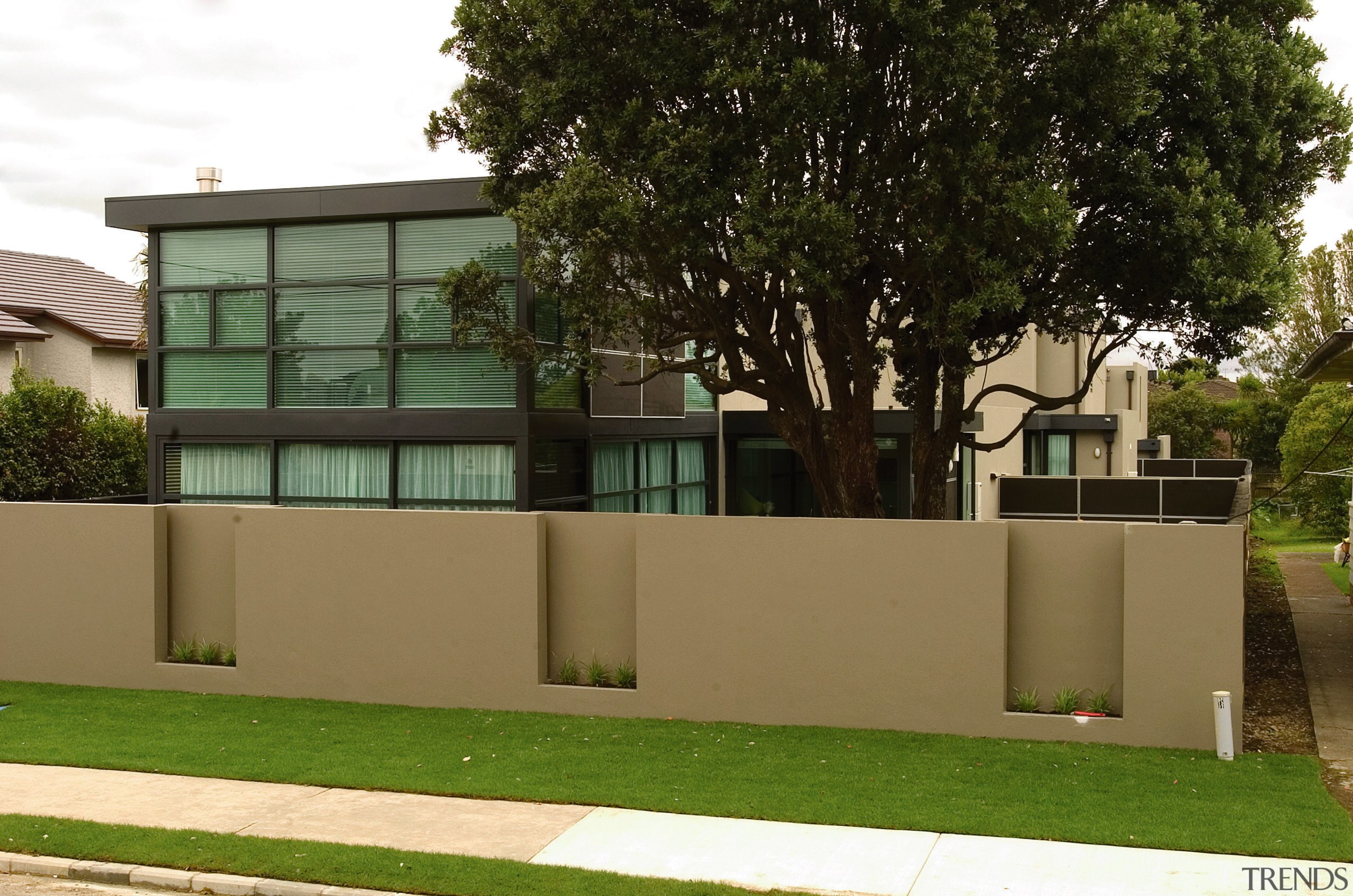 Street frontage of townhouse development with extensive glazing. architecture, building, facade, fence, grass, home, house, neighbourhood, plant, real estate, residential area, tree, brown