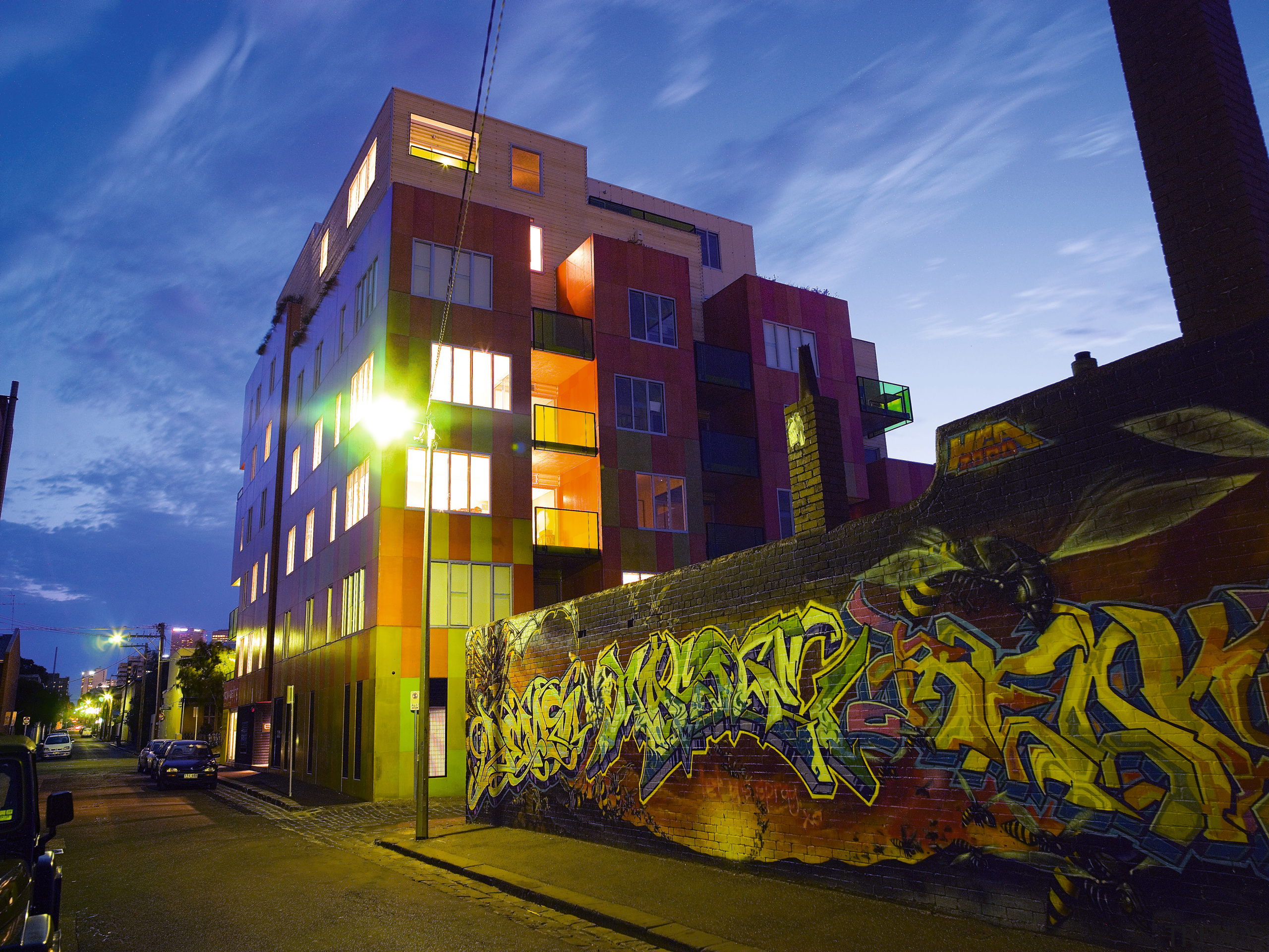 A view of this urban residential building implemented architecture, building, city, condominium, evening, facade, graffiti, house, landmark, metropolis, metropolitan area, mixed use, neighbourhood, night, real estate, residential area, sky, street, urban area, wall, yellow, blue, brown