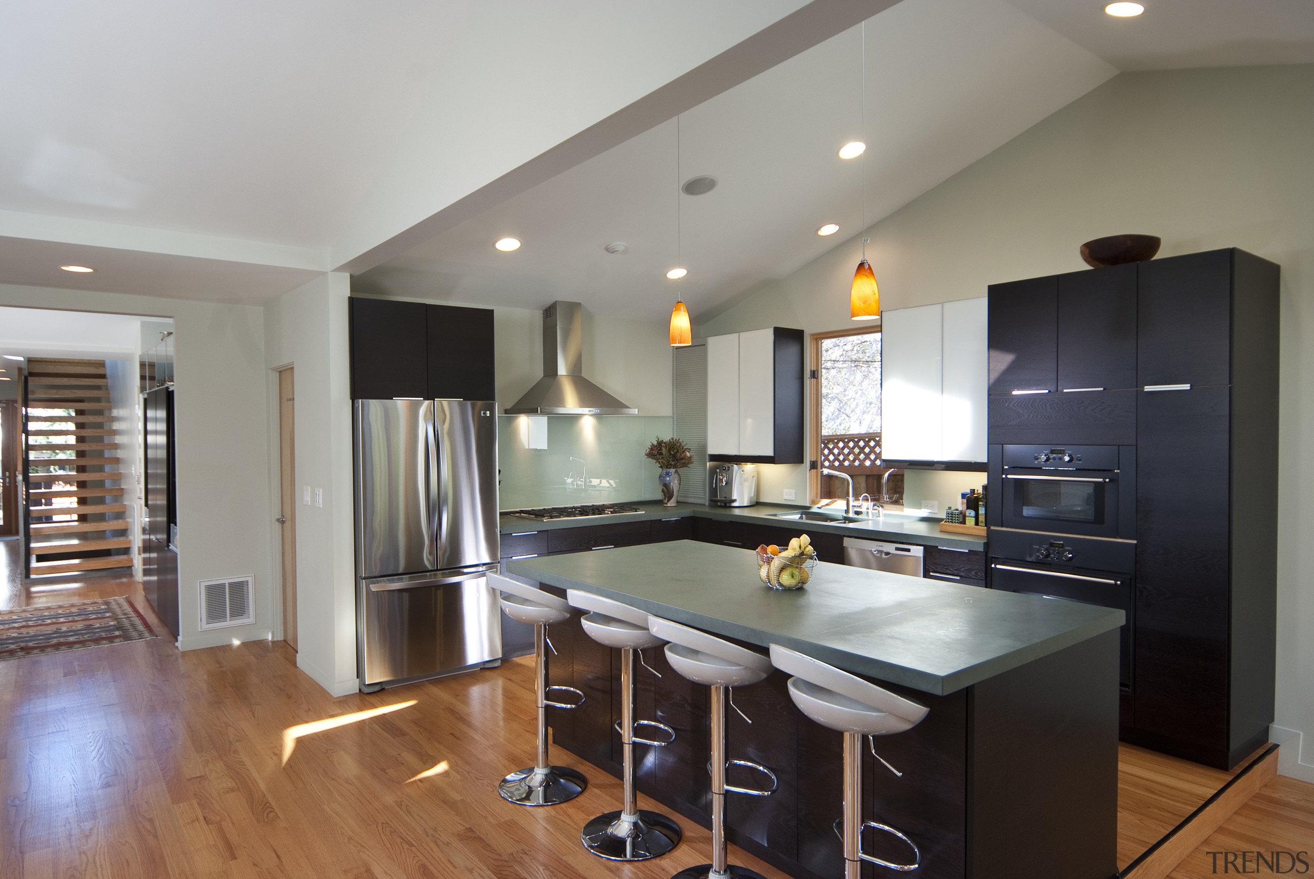 Kitchen with wooden flooring, dark island and stools. countertop, floor, flooring, hardwood, interior design, kitchen, living room, real estate, room, wood flooring, gray