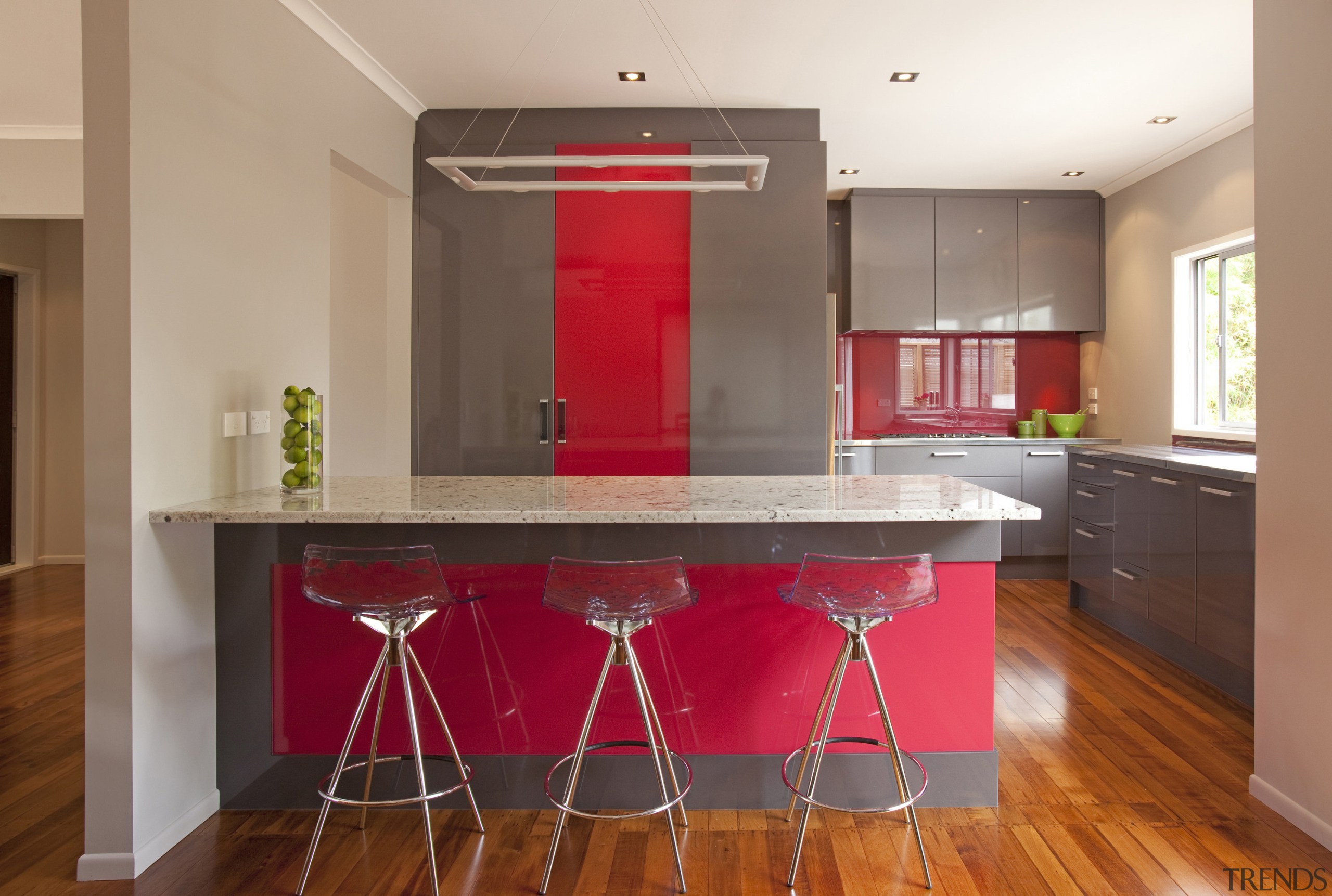 Streamlined grey kitchen with red accents. Peniinsula with cabinetry, countertop, floor, flooring, hardwood, interior design, kitchen, property, real estate, room, table, brown