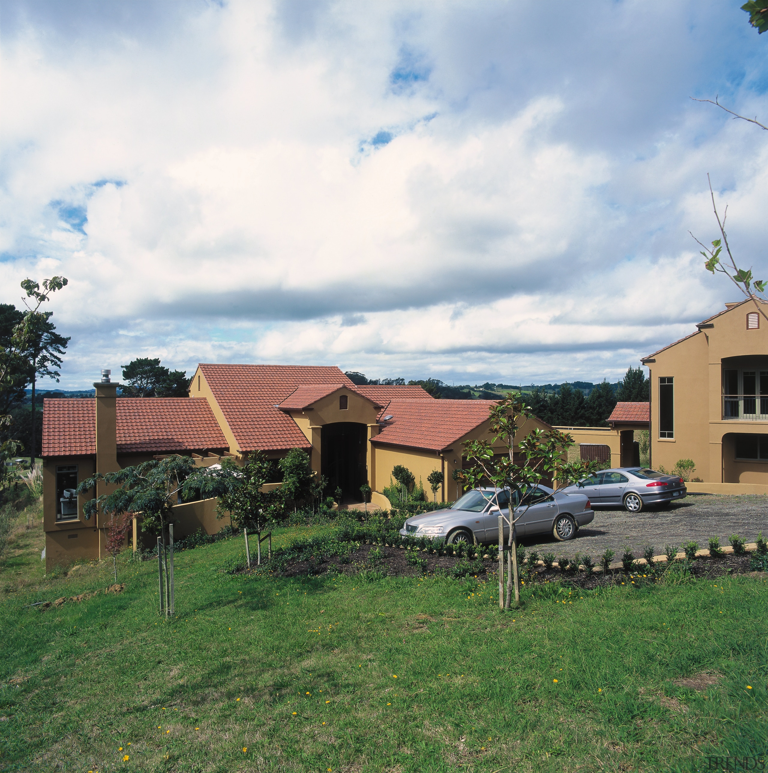 View of large home with terracotta coloured cladding area, cloud, cottage, estate, farm, farmhouse, home, house, land lot, landscape, neighbourhood, plant, property, real estate, residential area, roof, rural area, sky, suburb, tree, village, yard, white