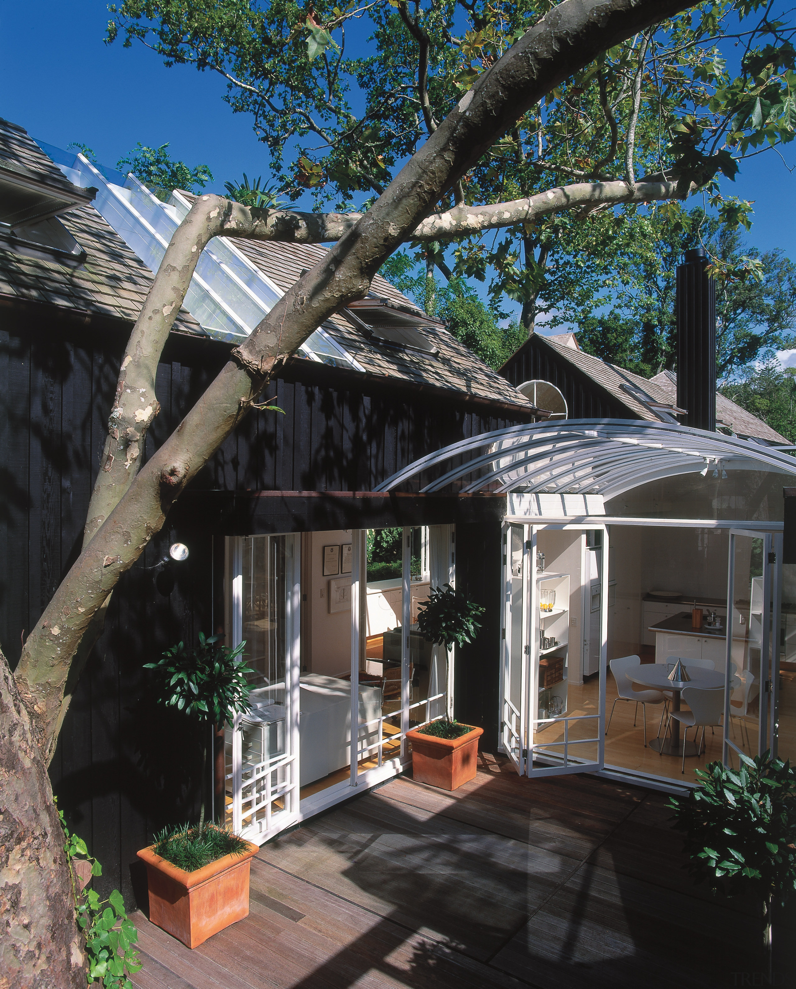 An exterior view of this home designed by architecture, cottage, home, house, outdoor structure, real estate, roof, siding, tree, black