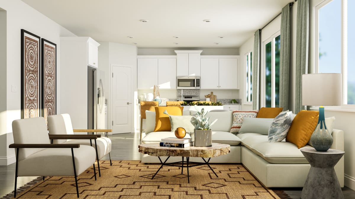 Staged rendering of great room with view into the kitchen, furnished with beige sofa, two armchairs, and coffee table.
