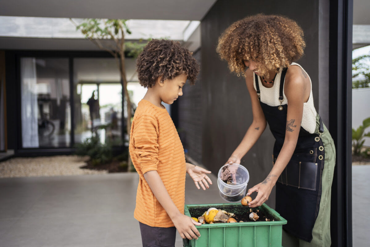 Young woman and her younger brother making compost from kitchen food leftovers into rich organic soil fertilizer.