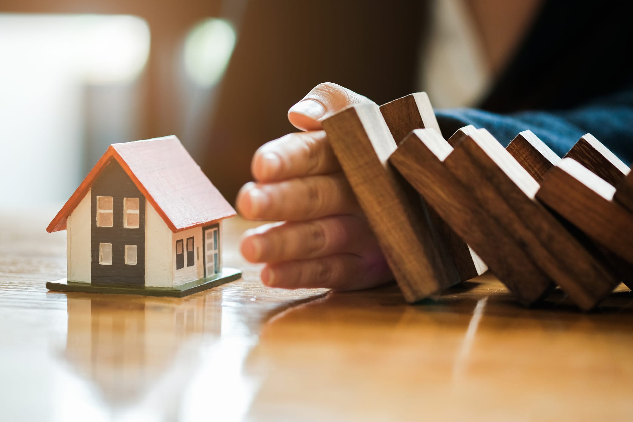 Close-up Of Business Woman Hand Stopping and Covering The Wooden Blocks From Falling On House Model, insurance concept.