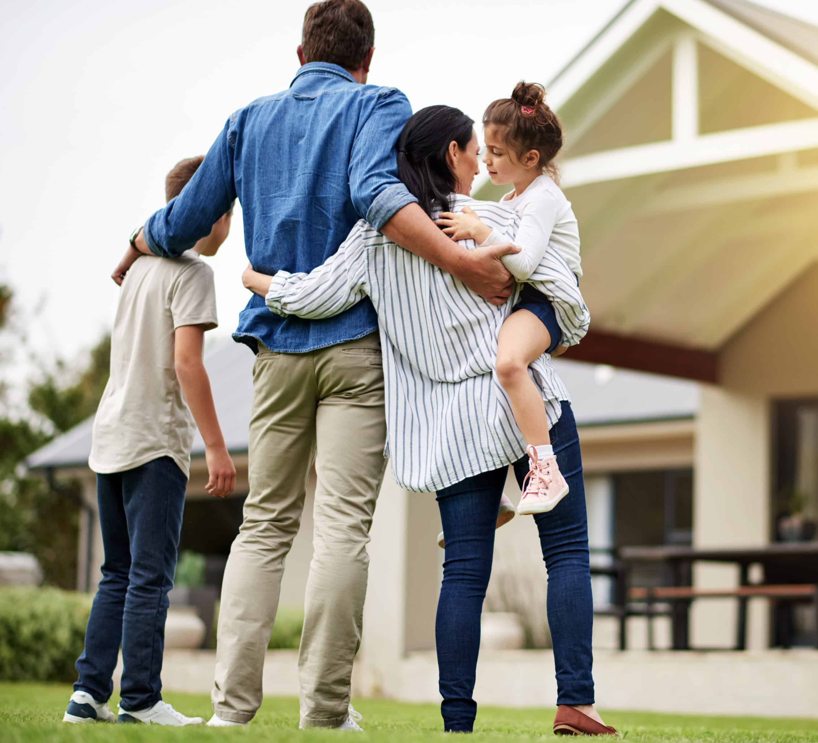 A family of four embracing in front of a house.