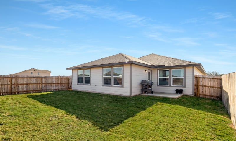 View of fully fenced backyard, green grass, and patio area.