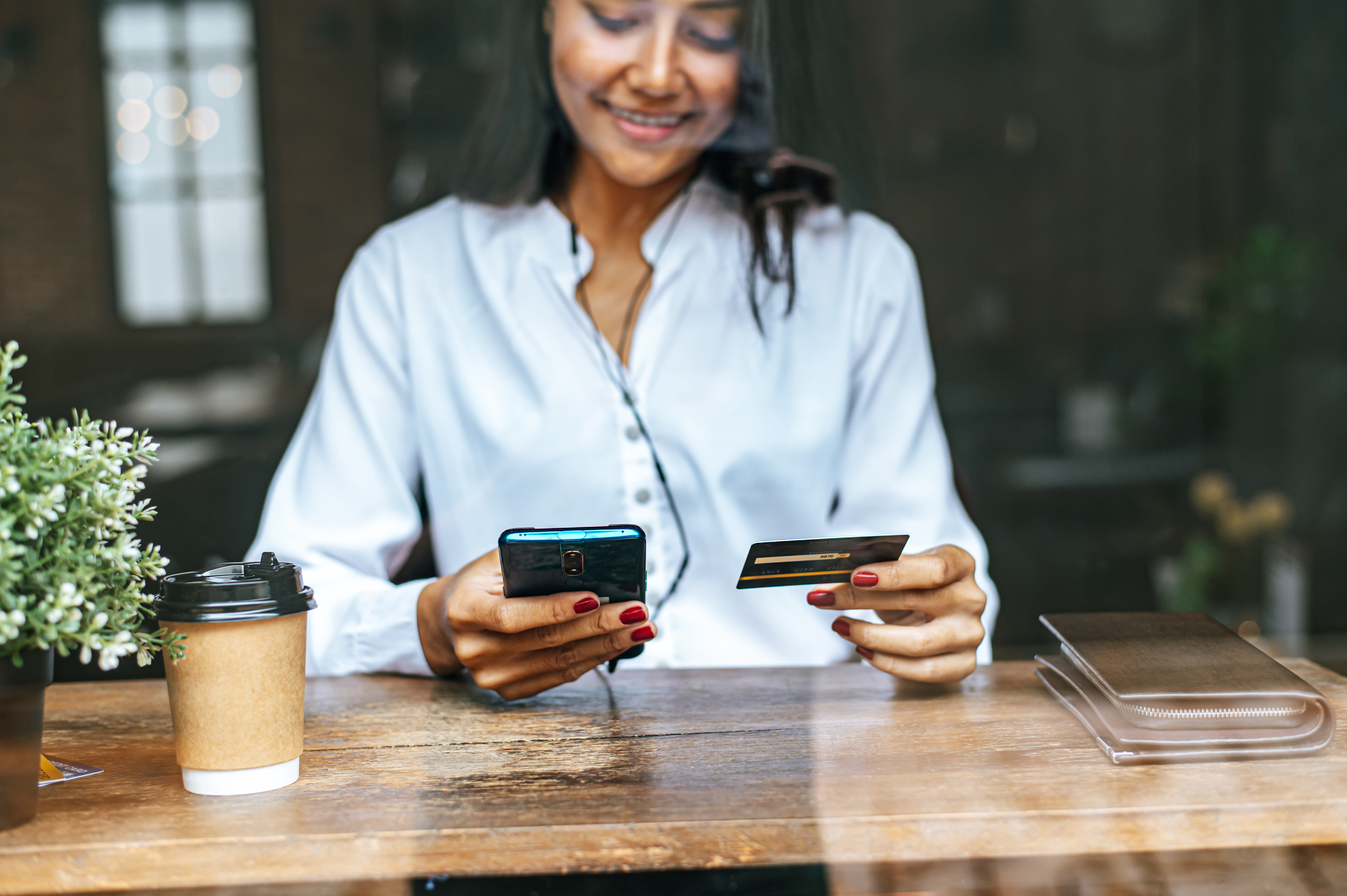 Femme assise dans un café regardant son smartphone et sa carte corporate