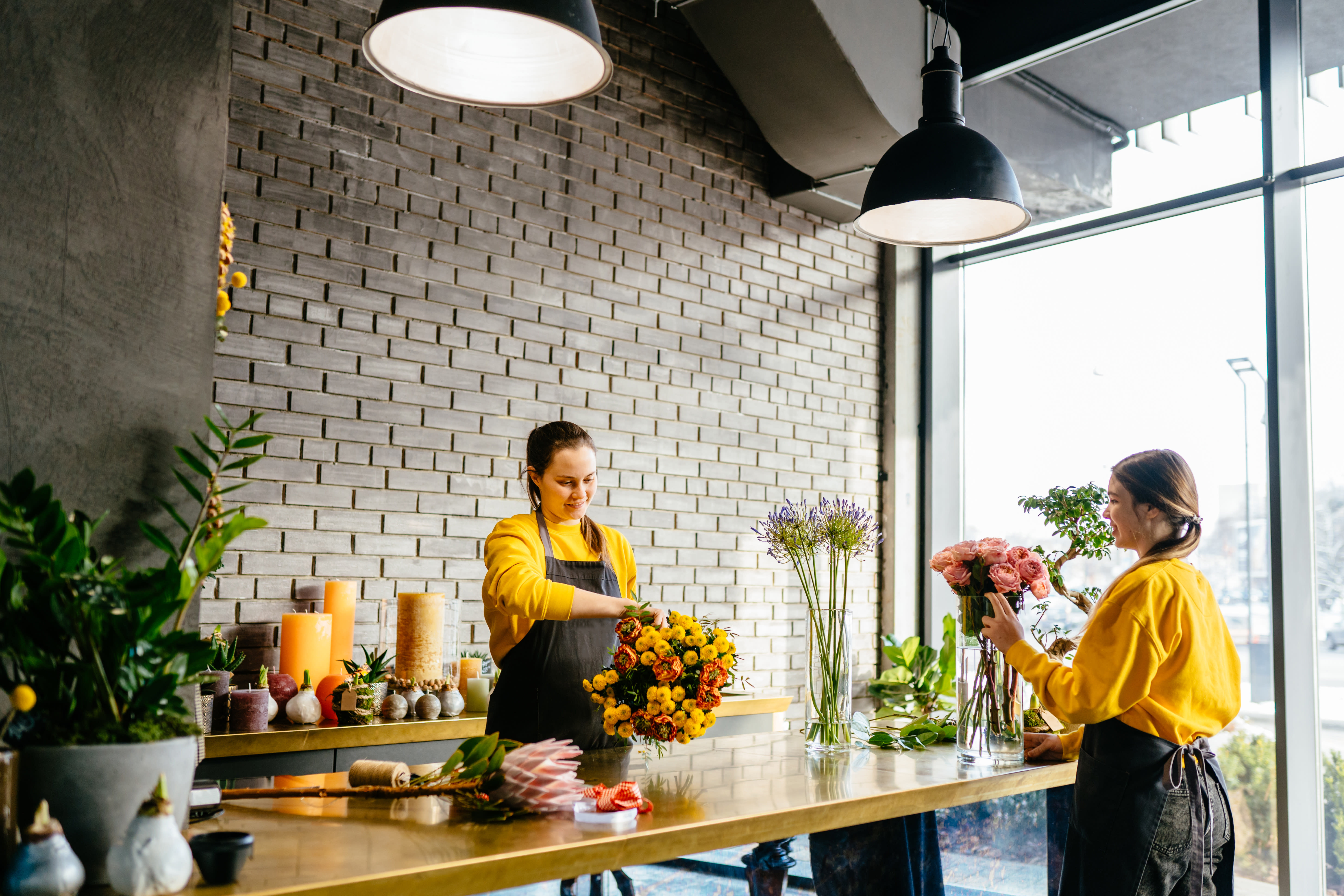 Image of women standing opposite one another with flower bouquets in hand arranging displays at florist 