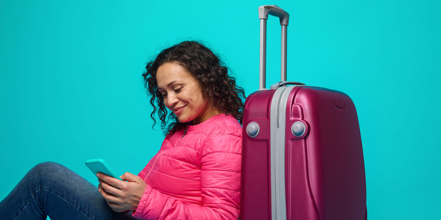 10 Best Business Travel Management Apps Hero - woman on cell phone next to rolling luggage