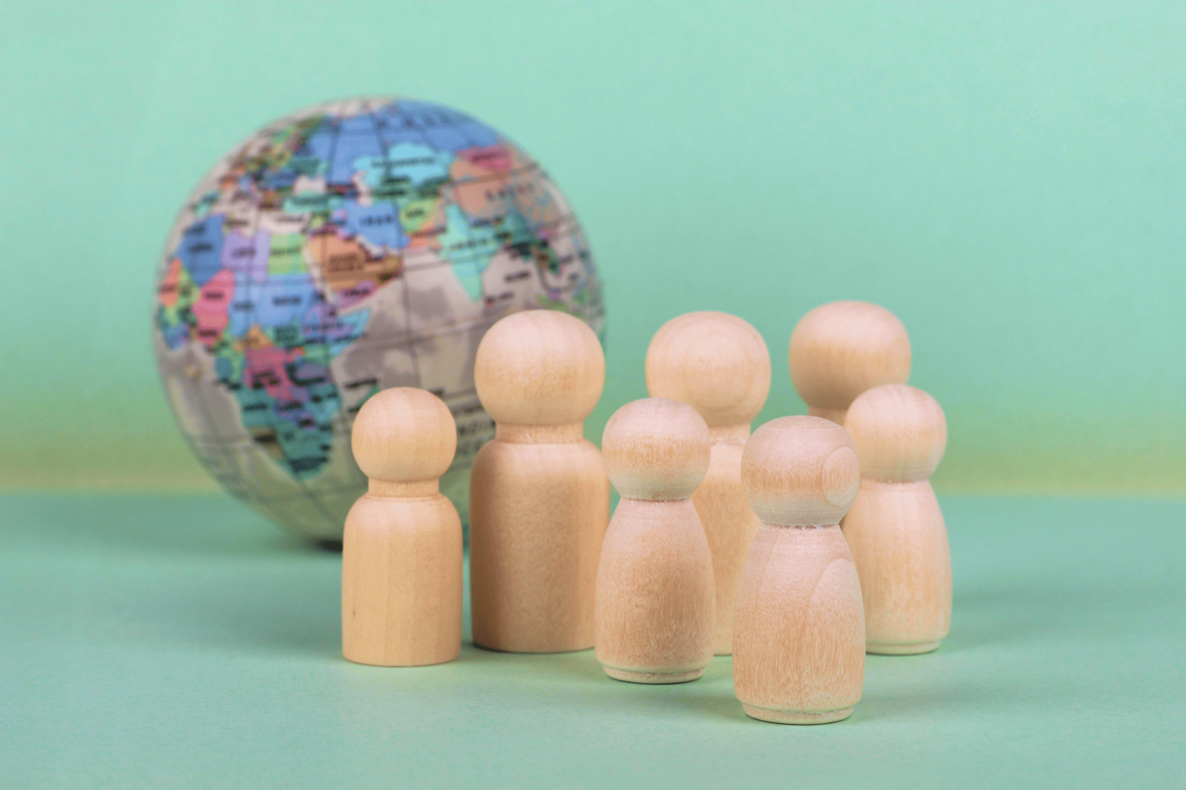 Holzfiguren vor einem Miniaturglobus, was die Fürsorgepflicht auf Geschäftsreisen symbolisiert