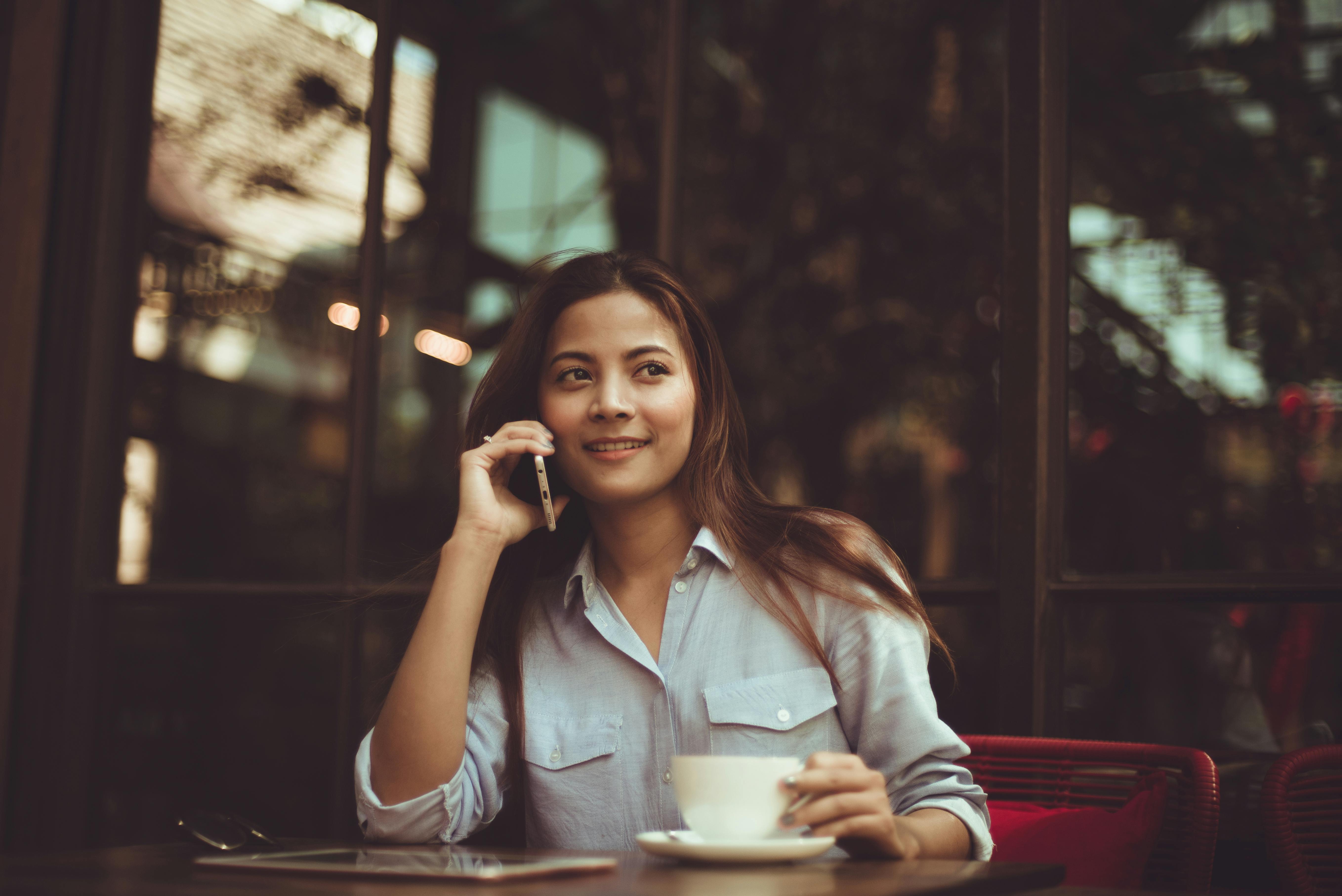 Frau, die auf einer Bleisure-Reise in einem Café sitzt und eine Tasse Kaffee trinkt, während sie telefoniert