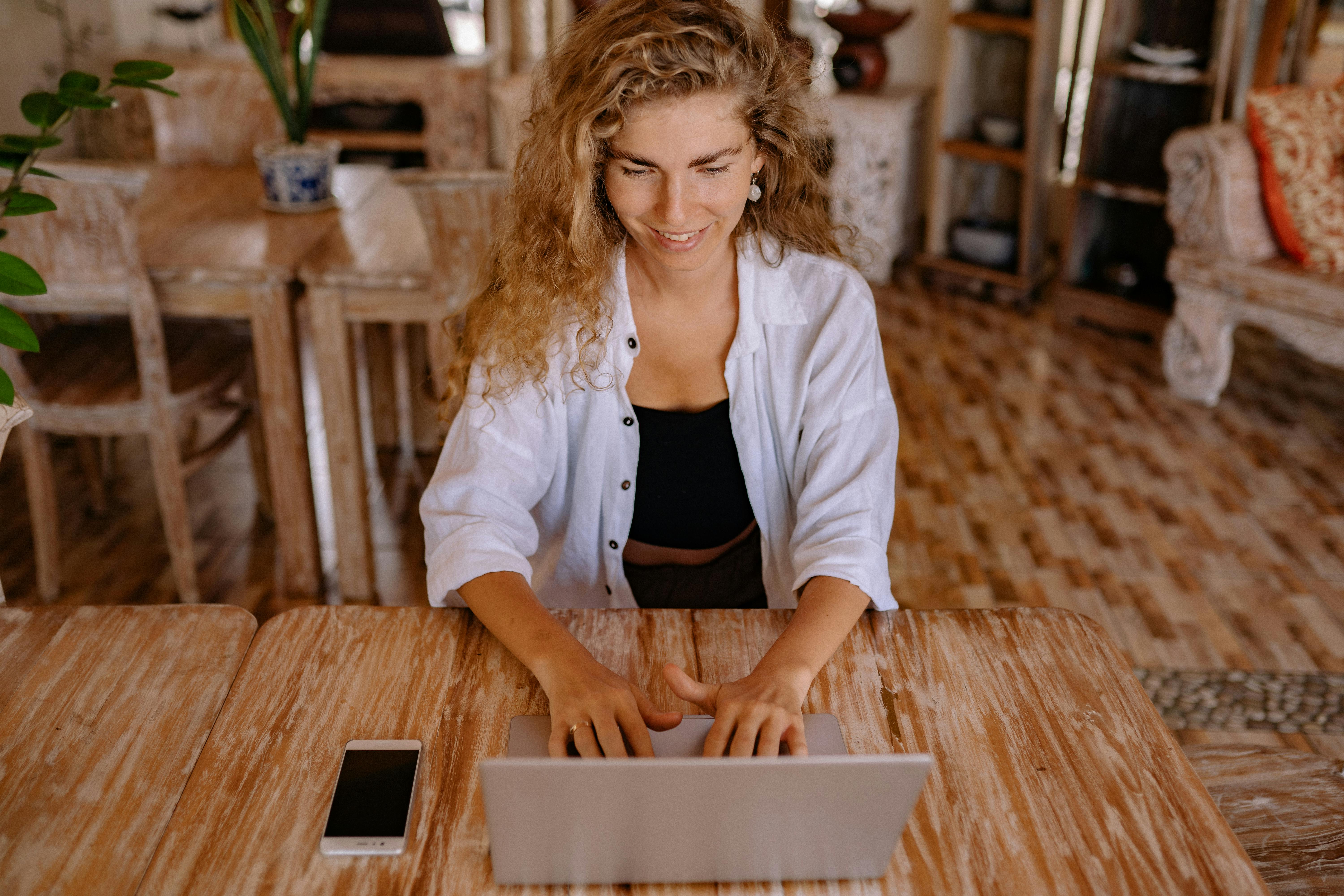 Glückliche Frau mit Laptop und Handy auf einer Workation