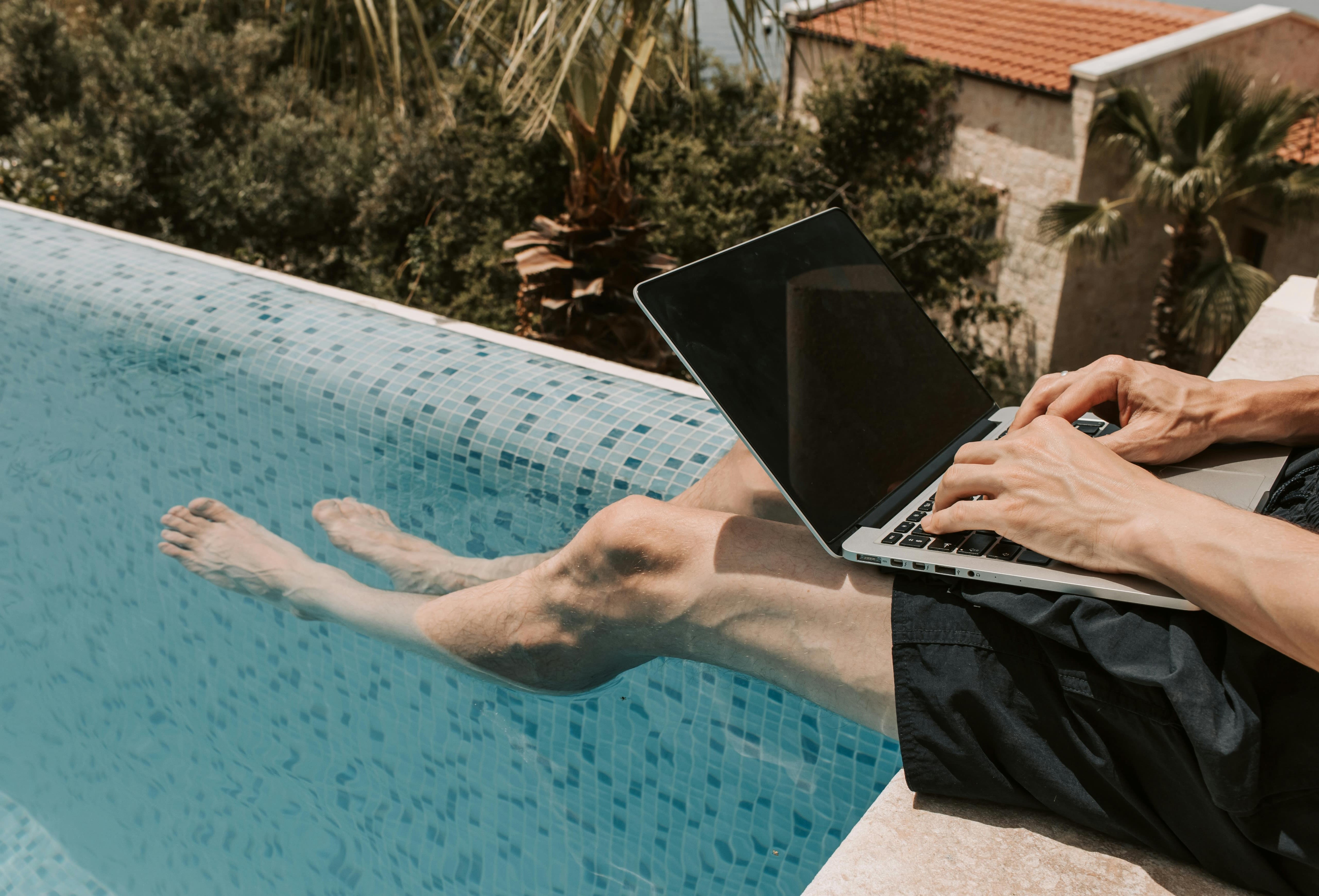 Mann am Pool, der während einer Workation mit dem Laptop arbeitet