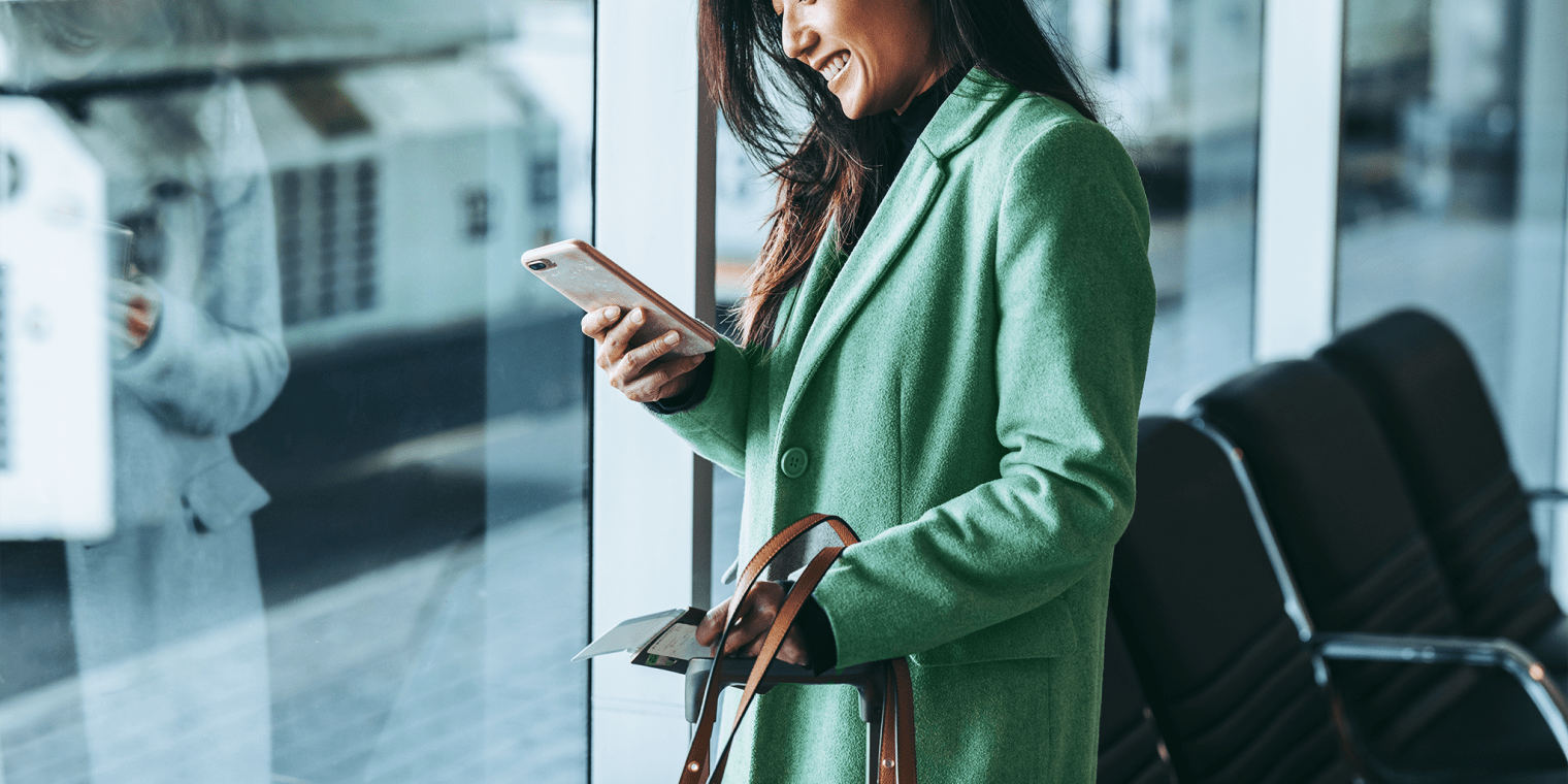 business class travel woman in airport looking at her phone smiling
