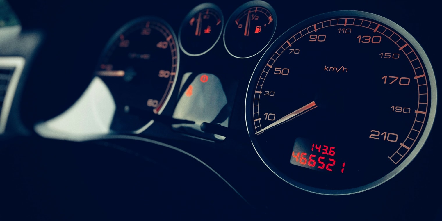 Tacho eines Fahrzeugs bei Nacht, der Kilometerstand und Fahrtgeschwindigkeit anzeigt.