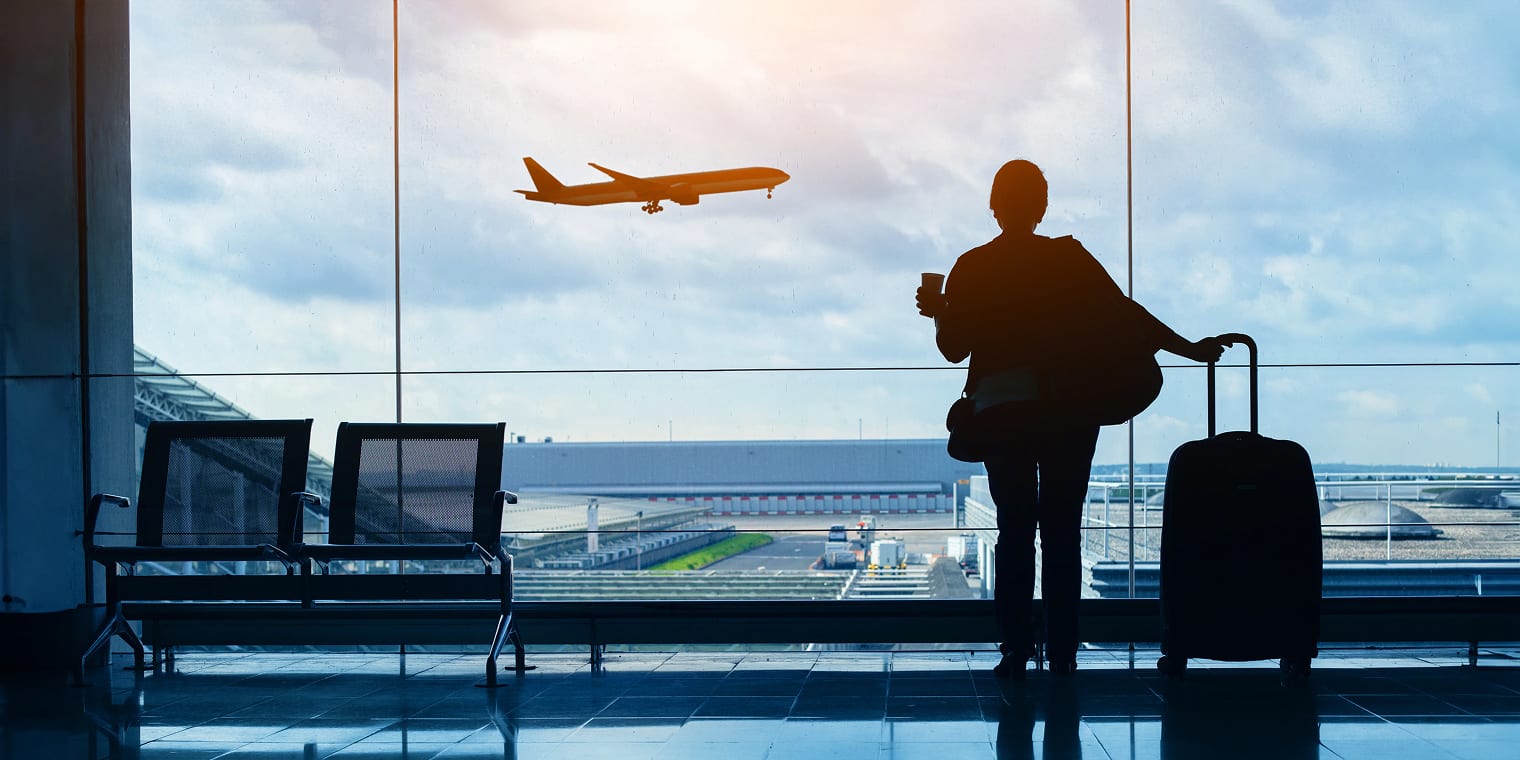 Eine Reisende am Flughafen, die entspannt in die Ferne guckt, weil sie durch ihr Unternehmen Sicherheit auf ihren Geschäftsreisen genießt.