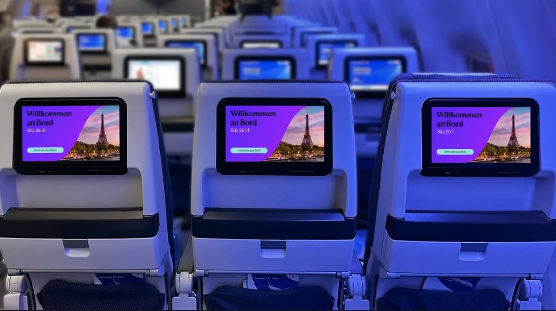 Sitzreihe im Flugzeug mit Bildschirmen, die Gäste bei der Inflight Series willkommen heißen