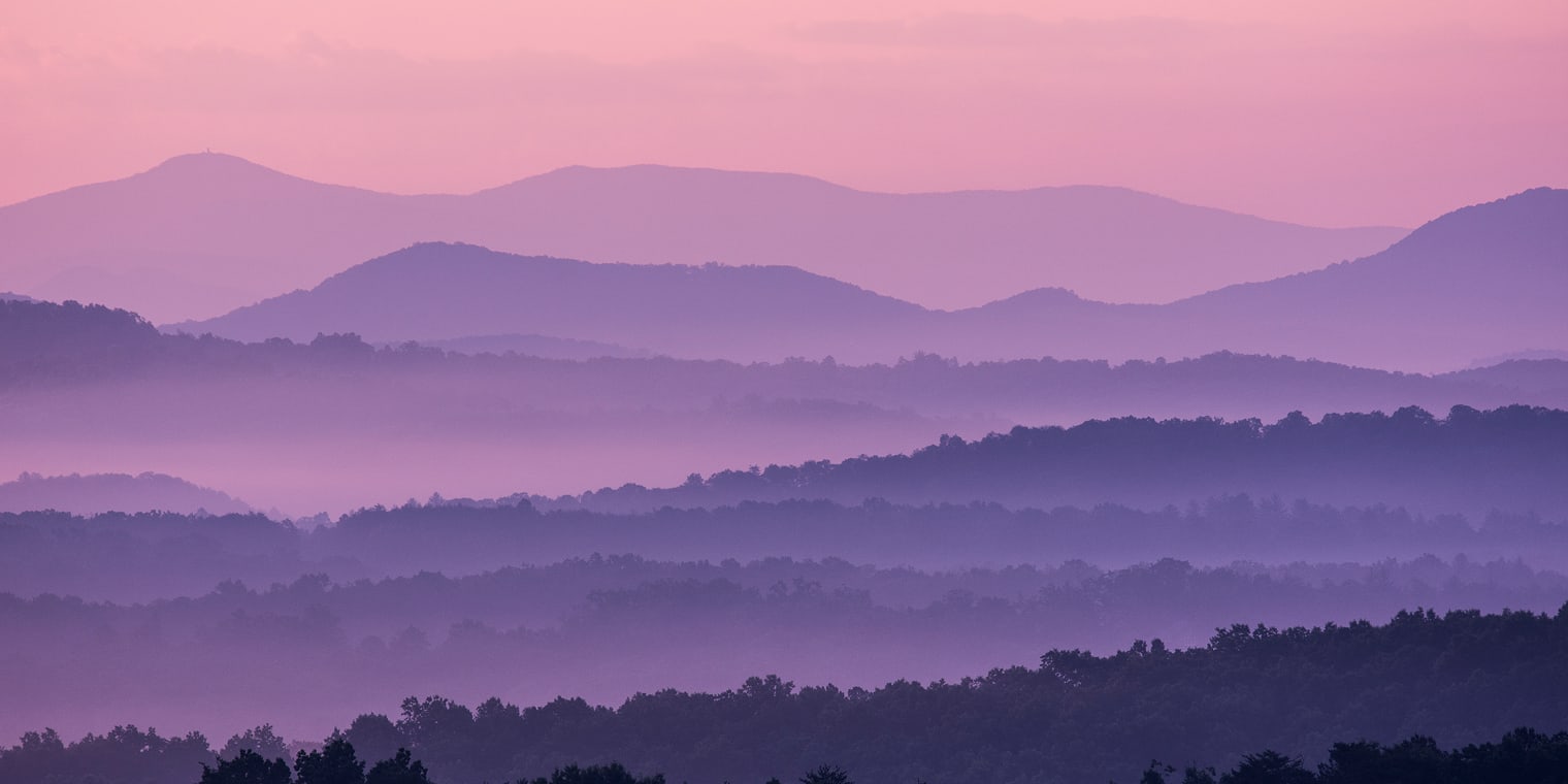 Layered mountain ridges in soft purple and pink hues at dawn. Like the structure and clarity of corporate travel policies