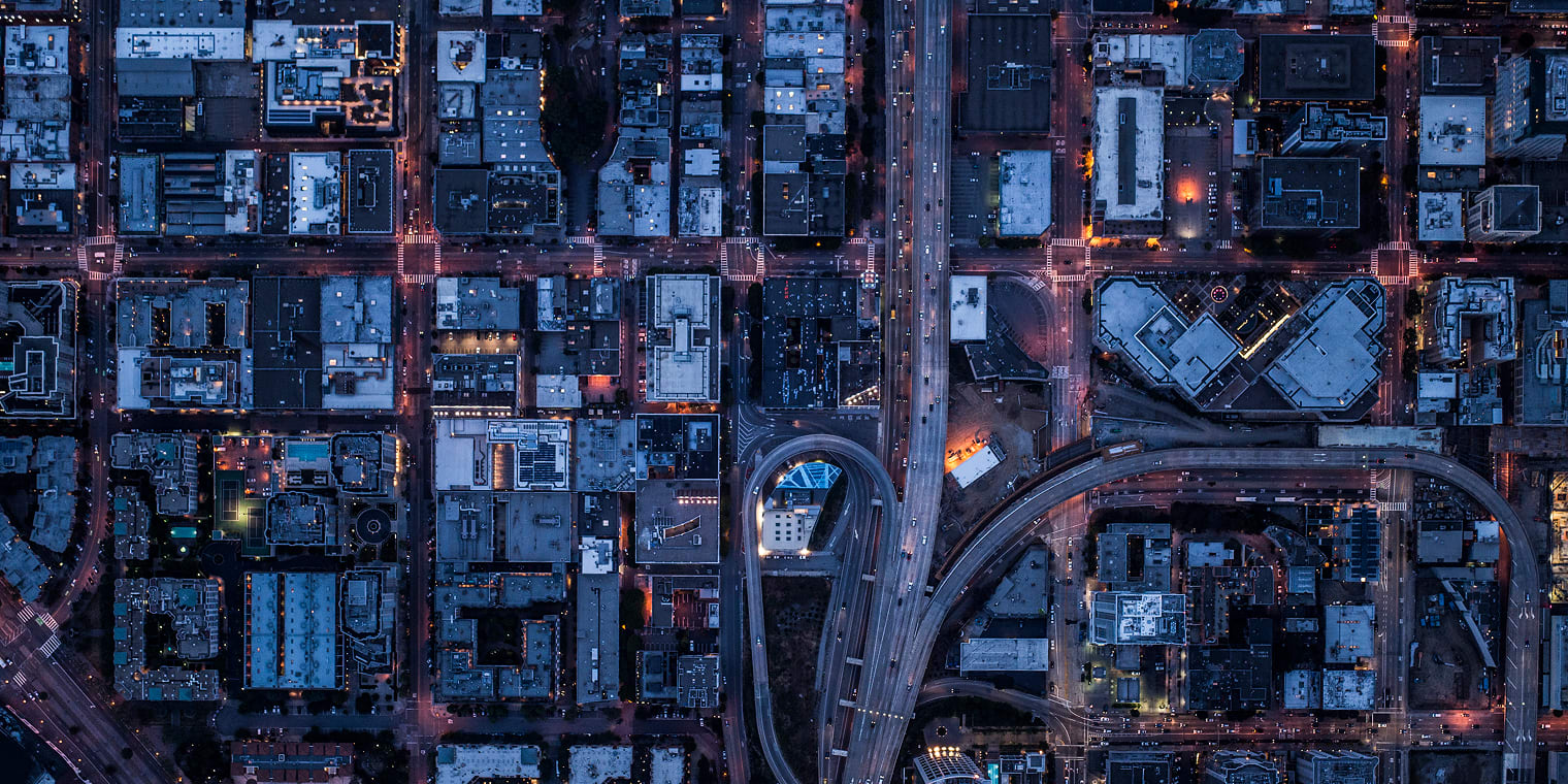 Aerial view of a city at dusk, with illuminated streets, high-rise buildings, and a winding highway. This urban landscape symbolizes the complexity of financial decisions in business, like choosing between a corporate card vs. P-Card