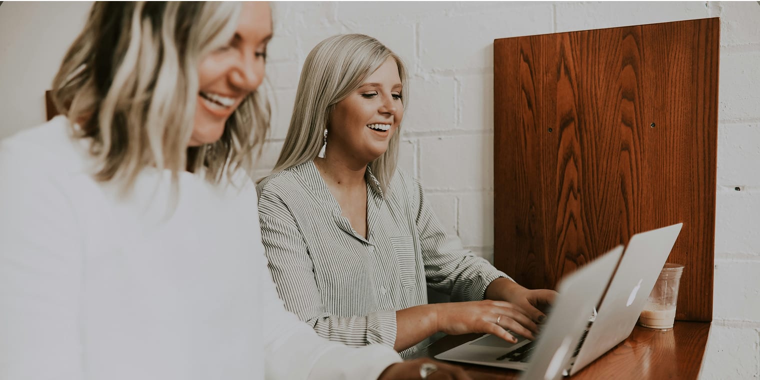 Zwei blonde Frauen arbeiten gemeinsam mit ihren Laptops an einem Projekt und fühlen sich von der Fürsorgepflicht gut betreut.