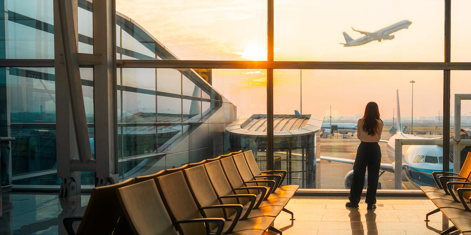 Woman at airport terminal looking at a plane during take-off. 
