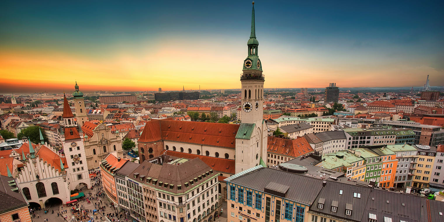 Panoramablick über die Münchner Altstadt bei Sonnenuntergang mit den markanten Kirchtürmen und den roten Dächern, unweit der Messe München.