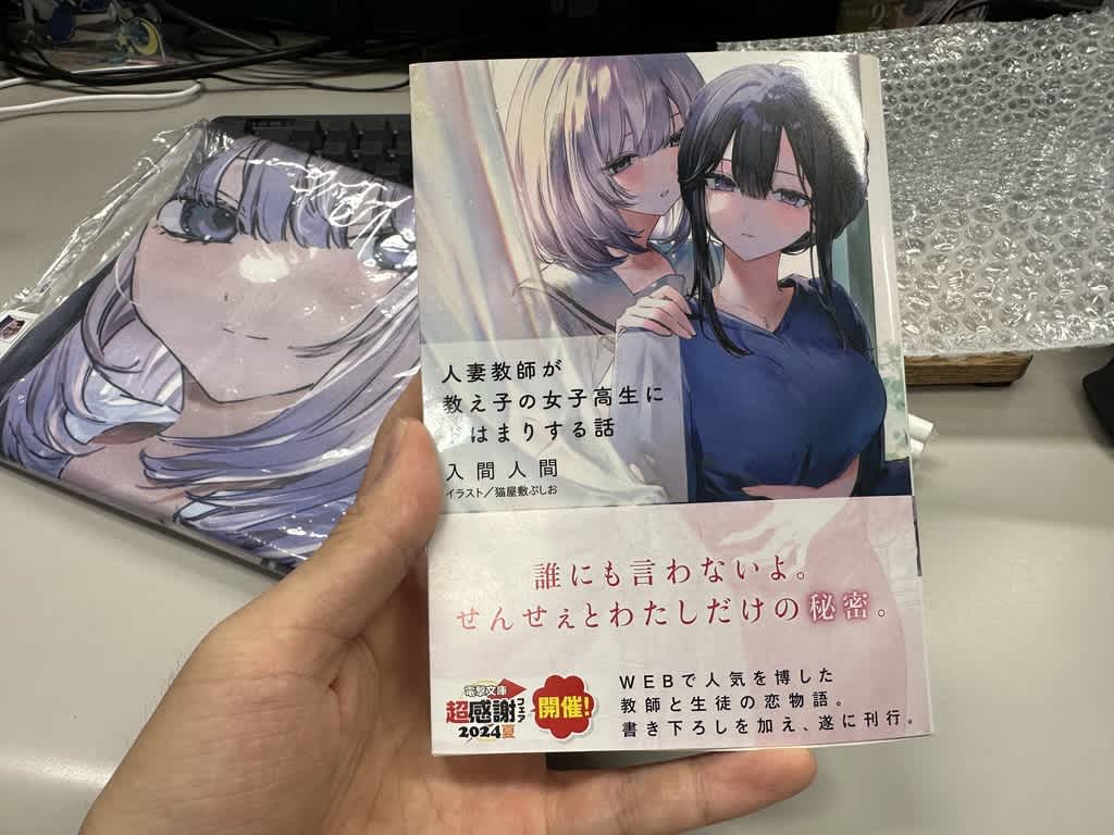 手に持った小説『人妻教師が教え子の女子高生にドはまりする話』の表紙