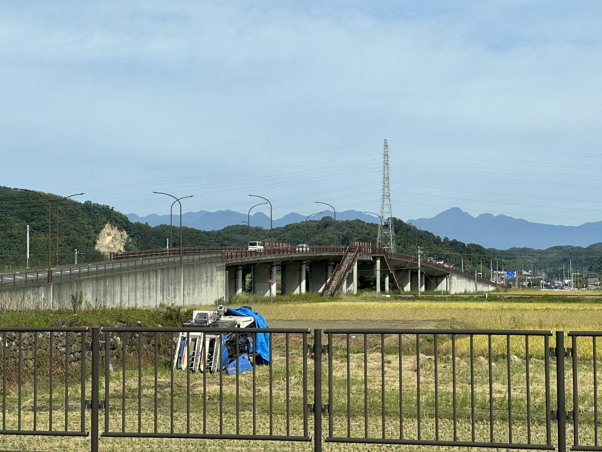 田んぼに大きな車道の橋がかかっていて、橋の中央から歩行者用の階段が出ている