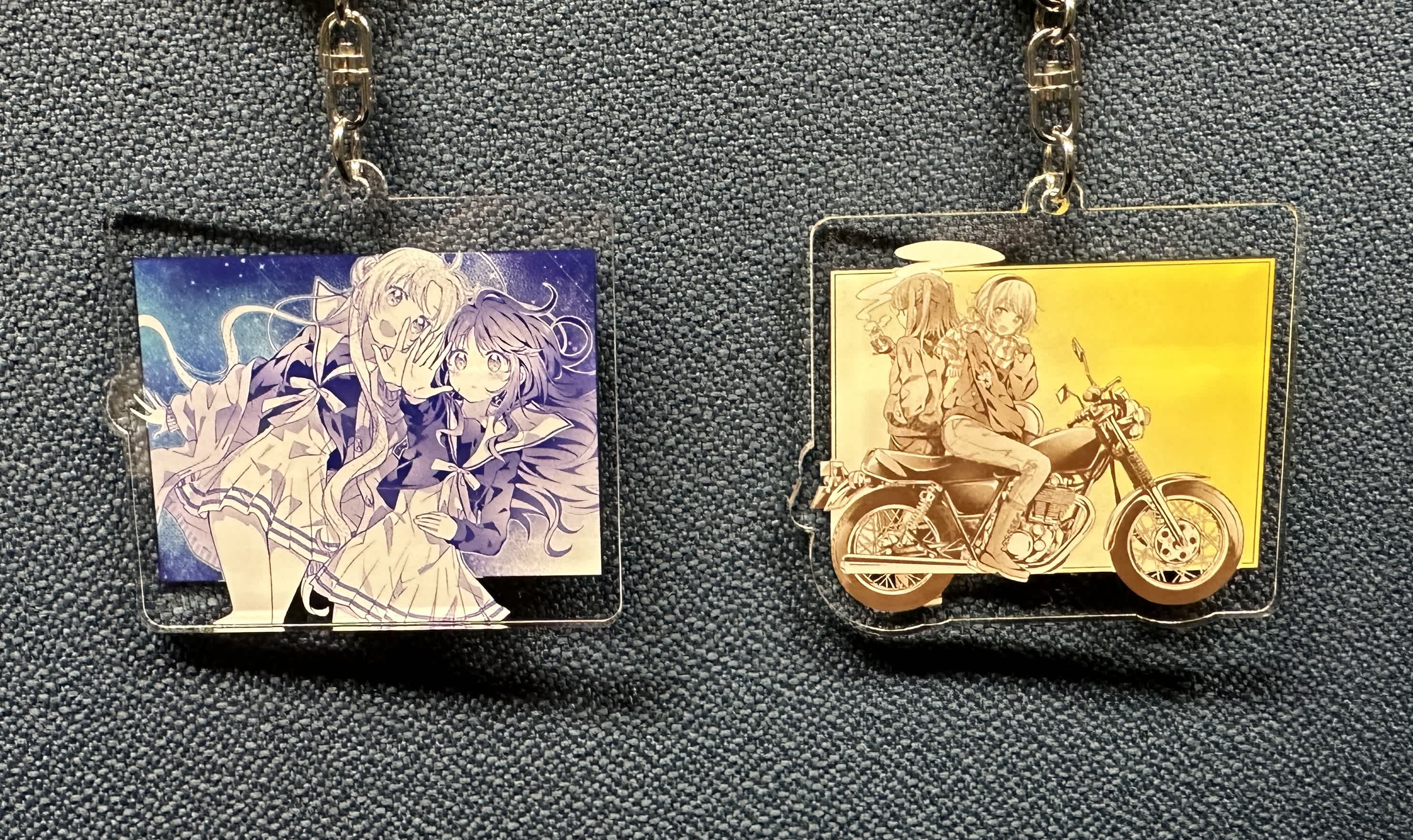 星屑テレパスのキーホルダー2個の画像。左側のキーホルダーには、明内ユウと小ノ星海果が星空の下で空に手を伸ばすシーンが描かれている。右側のキーホルダーには、雷門瞬と宝木遥乃がバイクに座るシーンが描かれている。