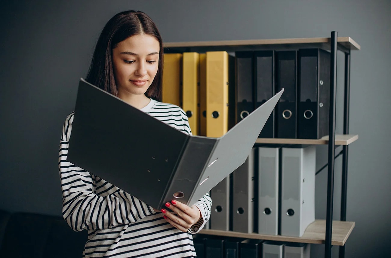 Someone reviewing a document folder in front of shelves of labeled binders