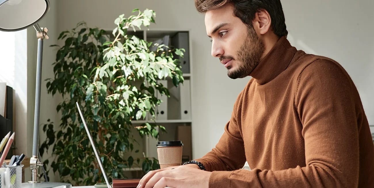 Person typing on a laptop at a bright desk with notebooks and a coffee cup
