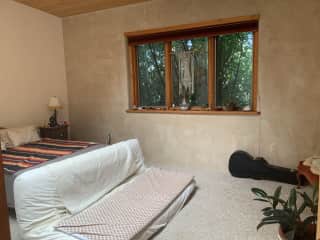Main bedroom - it’s big! Acequia is rushing outside the big window - you’ll always hear it! Giant skylight above. Organic latex queen mattress, extra blankets, organic bedding. At foot of bed is an additional queen futon with Biomat for your relaxation.