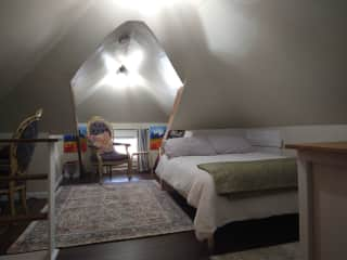 Third floor attic bedroom with full size bed, chair, and working table.