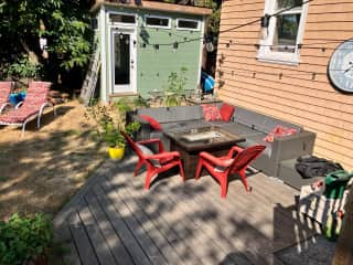 Ground level patio down stairs off the balcony with propane fire table. Green shed contains home gym equipment - treadmill, free weights, bench.