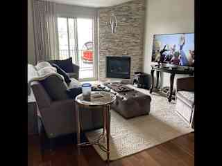 Living room with access to front balcony, & gas fireplace, with smart tv.