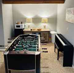 Family room in the basement with a foosball table,TV nook, snack bar and piano. The basement has a full bathroom with a tub and shower as well as two bedrooms.