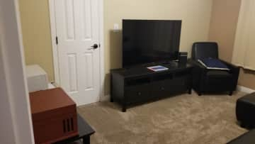 The second bedroom has a little microwave and refrigerator with a futon bed/couch and a chair. The window looks out onto the carport.