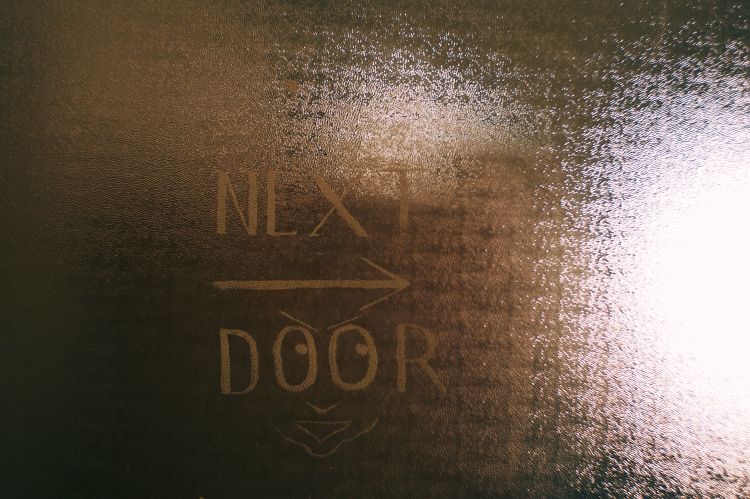 A glass panel on a door in The Nicholas Building, with a sign pointing to the right saying 'Next door'