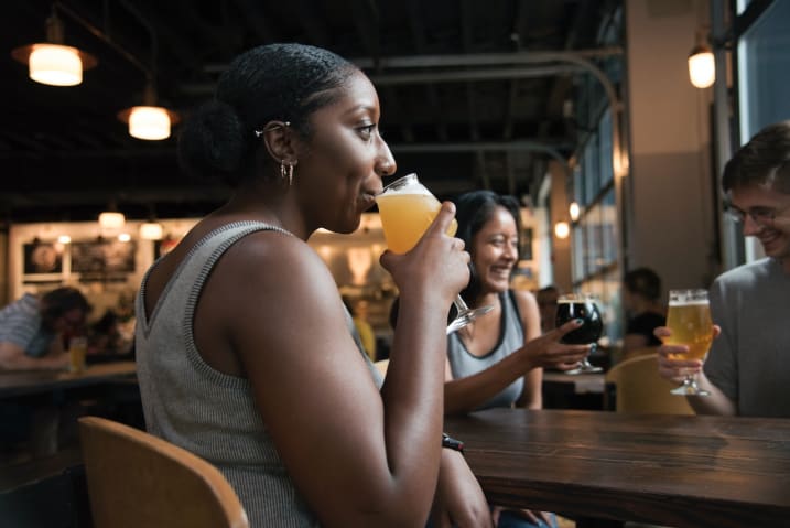 Photo of a woman at a restaurant sipping a beverage from a glass in the company of friends. Photo by ELEVATE from Pexels