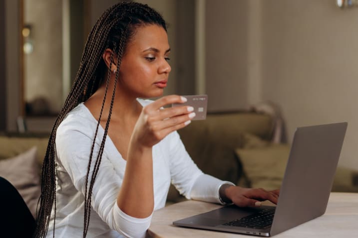 Photo of a woman holding a bank card while using her laptop computer. Photo by Mikhail Nilov from Pexels