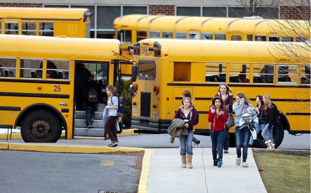half a dozen teenagers exiting their school busses and heading towards school, about to start the school day