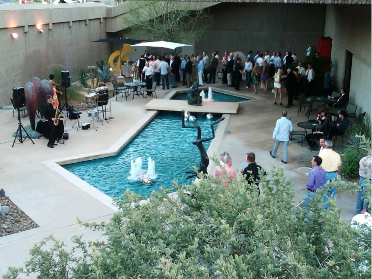 birds-eye view of about 50 guests gathered at an outdoor daytime reception  with live music, surrounding a clear blue decorative pool